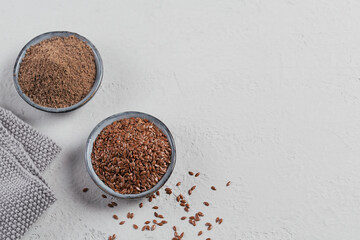 Brown flax seed and ground or crushed flaxseed or linseed in small bowl on light gray background.