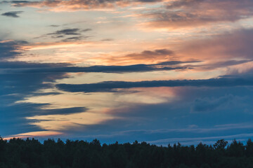 sunset sky with rural landscape; gloomy, dark view of the forest in the distance, sun-painted sky with clouds