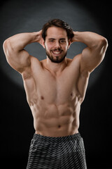 Fototapeta premium A handsome muscular man without a t-shirt poses for a photographer in a dark photo Studio. The concept of sport