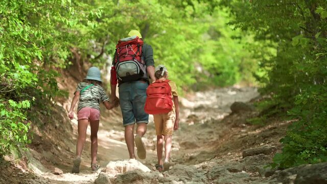Man with backpack walking with boy and girl. Travel lifestyle concept adventure outdoor summer vacations. Happy family hiking in the countryside. Father, son and daughter look and point to the forest