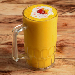 Mango Milkshake served in a glass over a rustic wooden background, selective focus on top