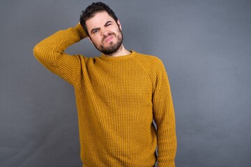Young handsome Caucasian man wearing yellow sweater against gray wall being confused and wonders...