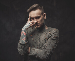 Dressed in ragged shirt stylish and bearded hipster with modern haircut poses in dark background