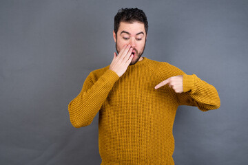 Shocked Young handsome Caucasian man wearing yellow sweater against gray wall look surprisedly...