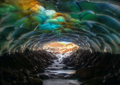Entrance in ice cave with colorful frozen ceiling and river. Kamchatka, Russia.