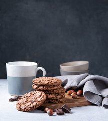 a stack of chocolate chip cookies with chocolate chips and  nuts with cup of tea  on a light table
