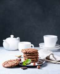 a  chocolate chip cookies with  nuts and mint with cup of tea and teapot  on a light table