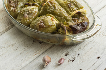 Pepper stuffed with white cheese, herbs, garlic. Glass dish prepared with seasonal local vegetables. White wood background