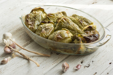 Pepper stuffed with white cheese, herbs, garlic. Glass dish prepared with seasonal local vegetables. White wood background