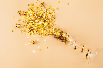 Glasses with golden confetti tinsel on beige background. Flat lay, top view, copy space. Celebrate party concept
