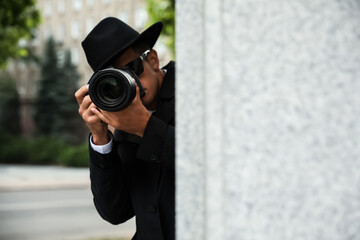 Private detective with modern camera spying on city street - obrazy, fototapety, plakaty