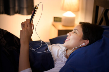 A young woman is using tablet , watching movies or video call to her friends or family in her bedroom , night Light.