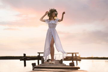 Fototapeta premium Young woman wearing wreath made of beautiful flowers on pier near river