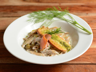 whole wheat penne pasta with salmon, zucchini, served in a white plate on a rustic wooden table, selective focus