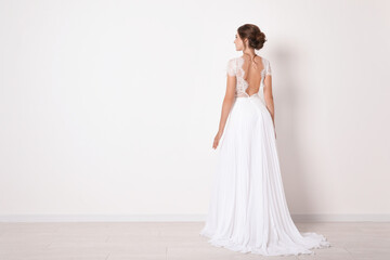 Fototapeta na wymiar Young bride wearing beautiful wedding dress near light wall. Space for text