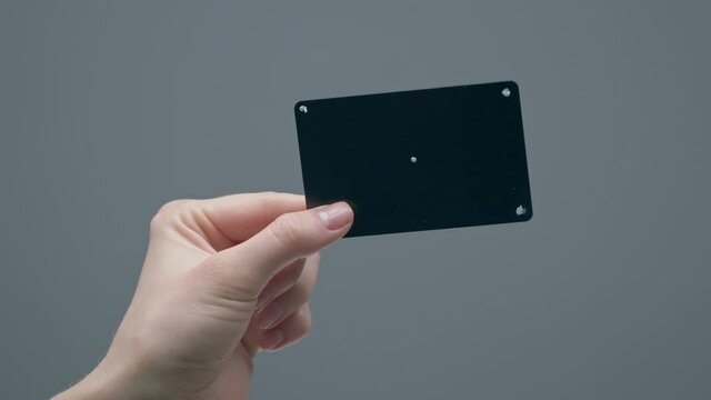 Black plastic bank card with tracking points in female hand on gray studio background, advertising video