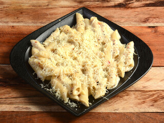 Penne pasta topped with a white creamy sauce and basil served in a plate on a rustic wooden table, selective focus