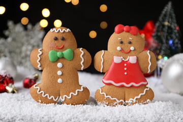 Gingerbread people on snow against festive lights, closeup