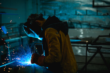 Welder in safety mask and glove using semi-automatic welding in workshop 