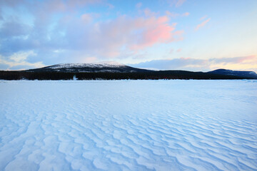 Ice pressure ridge on a frozen lake shore at sunset. Mountain peaks in the background. Colorful cloudscape. Picturesque winter scenery. Ecology, environment, climate change, global warming concepts