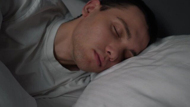 Calm handsome man goes to sleep in comfortable cozy fresh bed enjoying healthy good sleep nap.