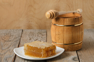 Honey in honeycomb on a white plate with a wooden jar and spoon on a rough wooden background.