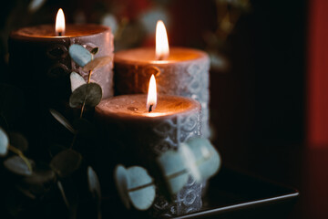 Black burning candles against dark red background with eucalyptus branch.