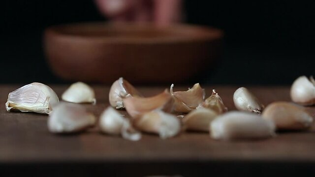 Throwing of garlic cloves from bowl on table, closeup