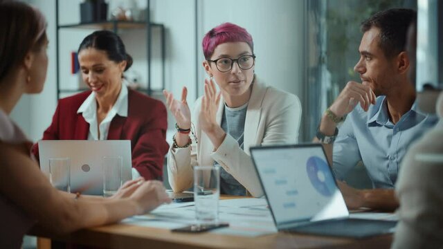 Office Meeting in Conference Room: Beautiful Specialist with Short Pink Hair Talks about Firm Strategy with Diverse Team of Professional Businesspeople. Creative Start-up Team Discusses Big Project 