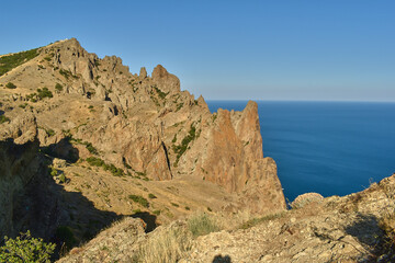 Beautiful landscape with rocks, green bushes on their slopes, sea and clear blue sky
