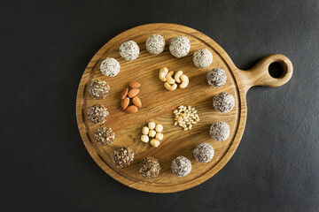 Raw vegetarian energy balls with cashews, hazelnuts, peanut butter and almond in wooden board top view on dark background. Vegetarian, organic food.