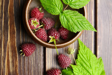 Fresh raspberry red berries with green leaves in bowl on wooden table