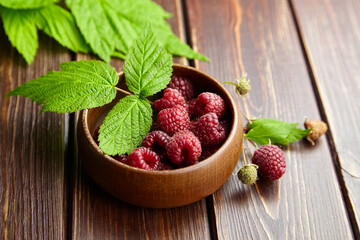 Fresh raspberry red berries with green leaves in bowl on wooden table