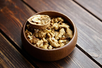 Walnuts in round bowl on wooden table. Half of walnut and dry seeds