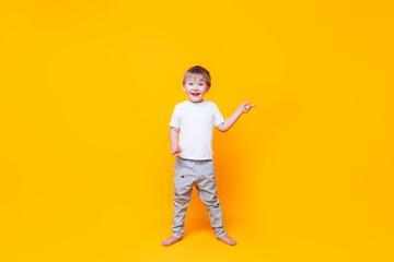 Cute boy on yellow background points with his hand to the side, photo for advertising product. color year 2021 illuminating and gray.