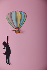 silhouette of a little girl with a colorful flying balloon on a pink background