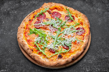 Pizza with cheese, sausage and arugula, on a wooden board, on a dark background