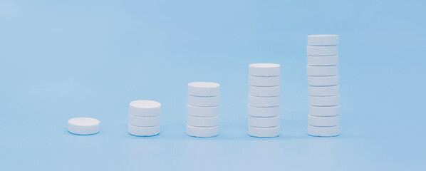 A stack of pills on a blue background. Growth graph made of stacked white pills