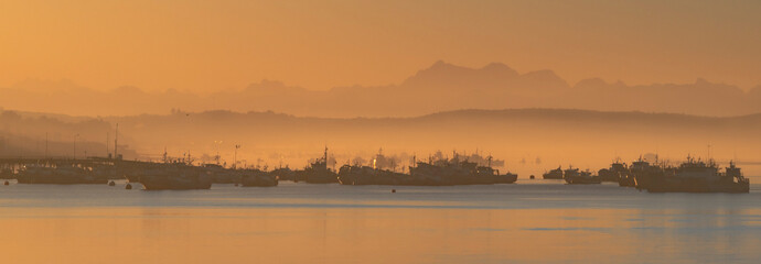 panoramic view of fishing boats in the mist of sunrise with mountains in the background