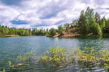 Lake with blue water and turquoise hue with banks in bright spring green against the sky with Cumulus clouds.