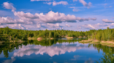 Fototapeta na wymiar Lake with banks in the bright spring green of the forest with a reflection of the blue sky with clouds in clear water.