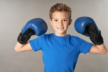 Cute boy in boxing gloves standing against gray background
