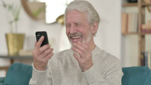 Portrait of Old Man Celebrating on Smartphone at Home 