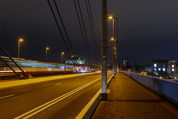 Plakat Night scenery of public transportation trams or train with motion blur and pedestrian pathway on suspension bridge without vehicle and traffic in Düsseldorf, Germany.