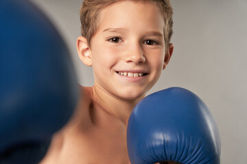Cheerful boy in boxing gloves standing against gray background