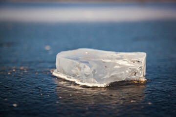 A piece of ice lies on the frozen water of the reservoir, melts and sparkles in the sun. Hard snow with a surface crust.