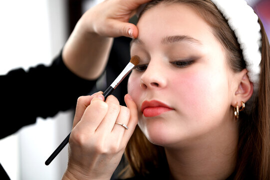 teen girl make up in a beauty salon. Young caucasian woman with make up brush near her face