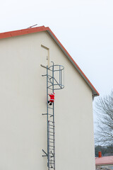 Christmas decoration on the side of a house. Inflatable Santa Clause climbing up a ladder...