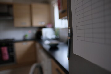 Pencil hanging on the front of the fridge, paper table stuck on the fridge door. Tracking groceries and writing down things that have to be purchased. Concepts planning ahead a schedule for the family
