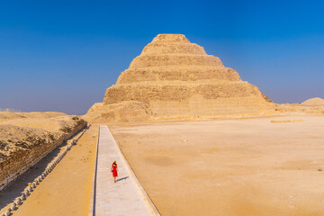 A young girl in a red dress walking in the Stepped Pyramid of Djoser, Saqqara. Egypt. The most important necropolis in Memphis. The first pyramid in the world